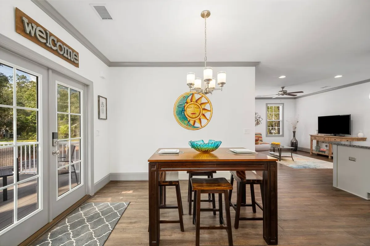 This image features a bright, welcoming dining area with a distinctive 'welcome' sign, a dining table, sun-themed wall art, and warm light fixtures. The scene gives off a sense of gathering and hospitality, suggesting shared meals and friendly conversations.