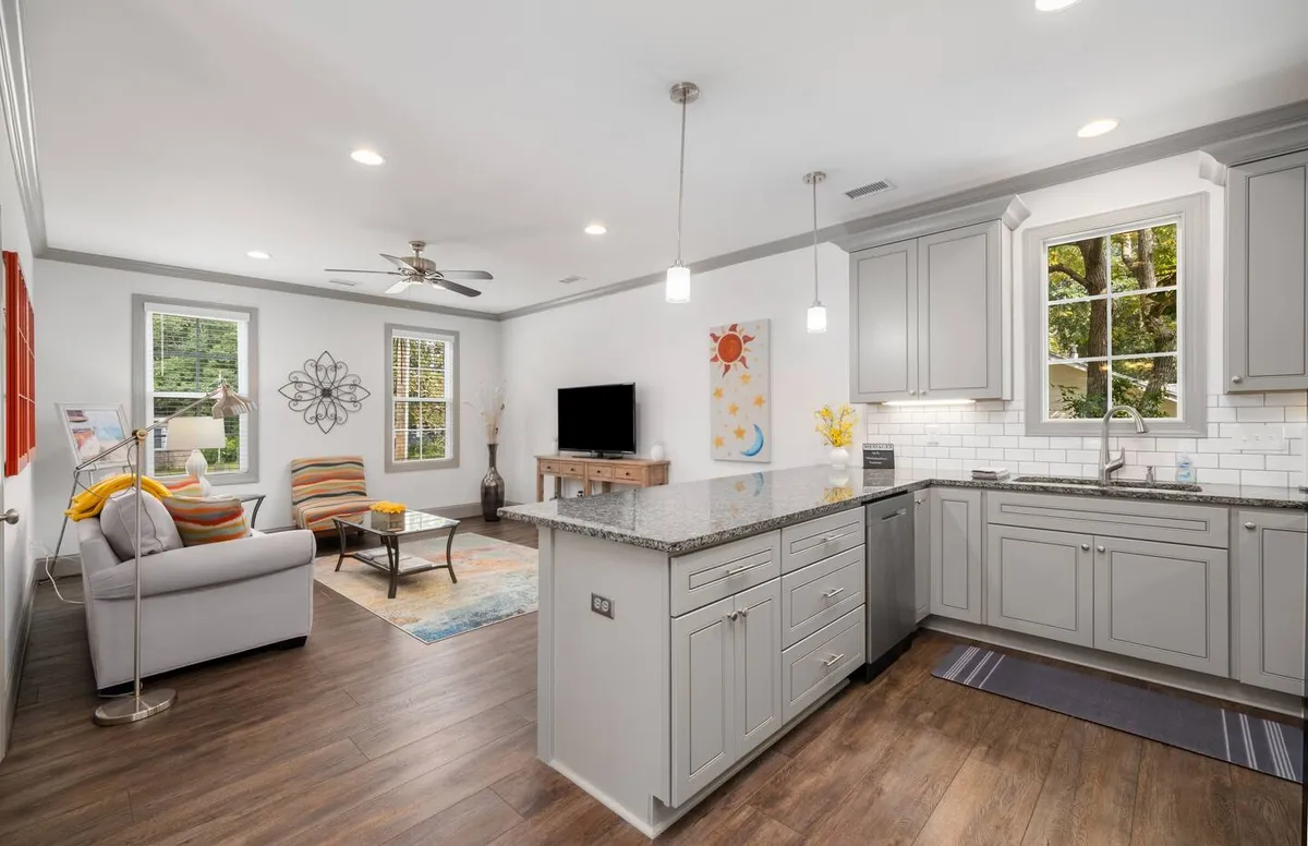 A cozy, open-concept living and kitchen space featuring a modern sofa, a contemporary coffee table, a kitchen island, decorative artwork, and large windows letting in sunlight. The layout emphasizes a seamless flow between relaxation and dining areas, echoing the section's emphasis on versatility and connection.