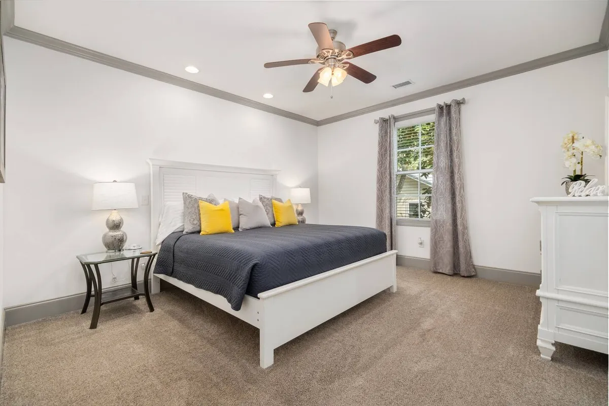 A serene bedroom with a bed dressed in gray and yellow accent pillows, a nightstand with a lamp, and a window with gentle natural light flowing in. The space feels cozy and restful, ideal for recharging after a day out.