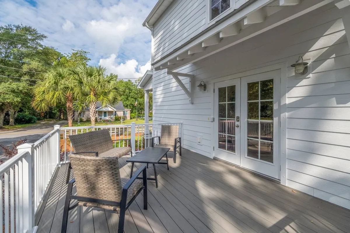 An inviting outdoor area with deck chairs and a small table set against a backdrop of palm trees and the facade of the house. The area is bathed in soft natural light, suggesting an atmosphere perfect for relaxing, reading, or socializing while enjoying the fresh air and greenery.