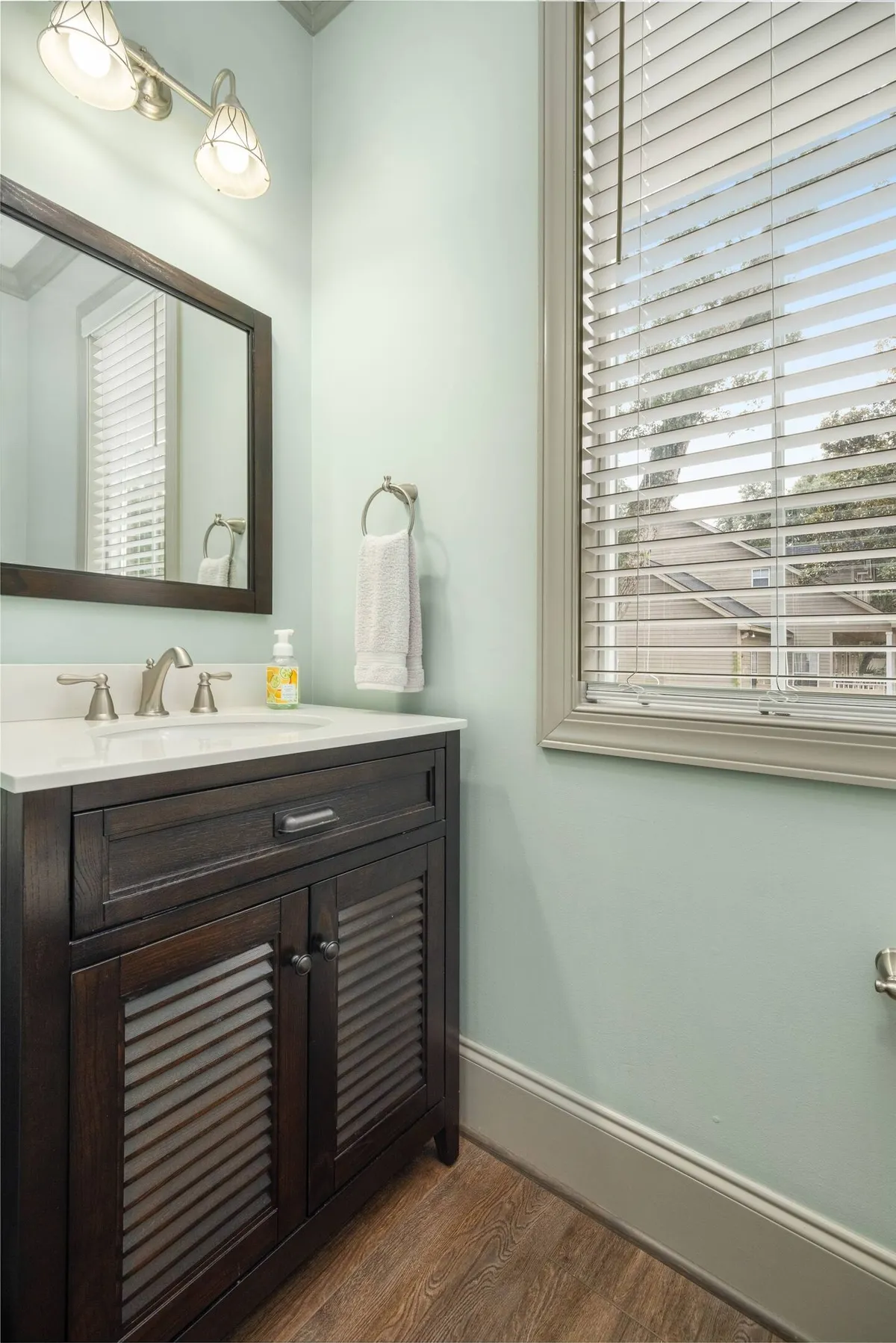 A bright and clean powder room with a vanity, sink, mirror, light fixtures, and a towel rack. The space is fresh and practical, perfect for getting ready or winding down.
