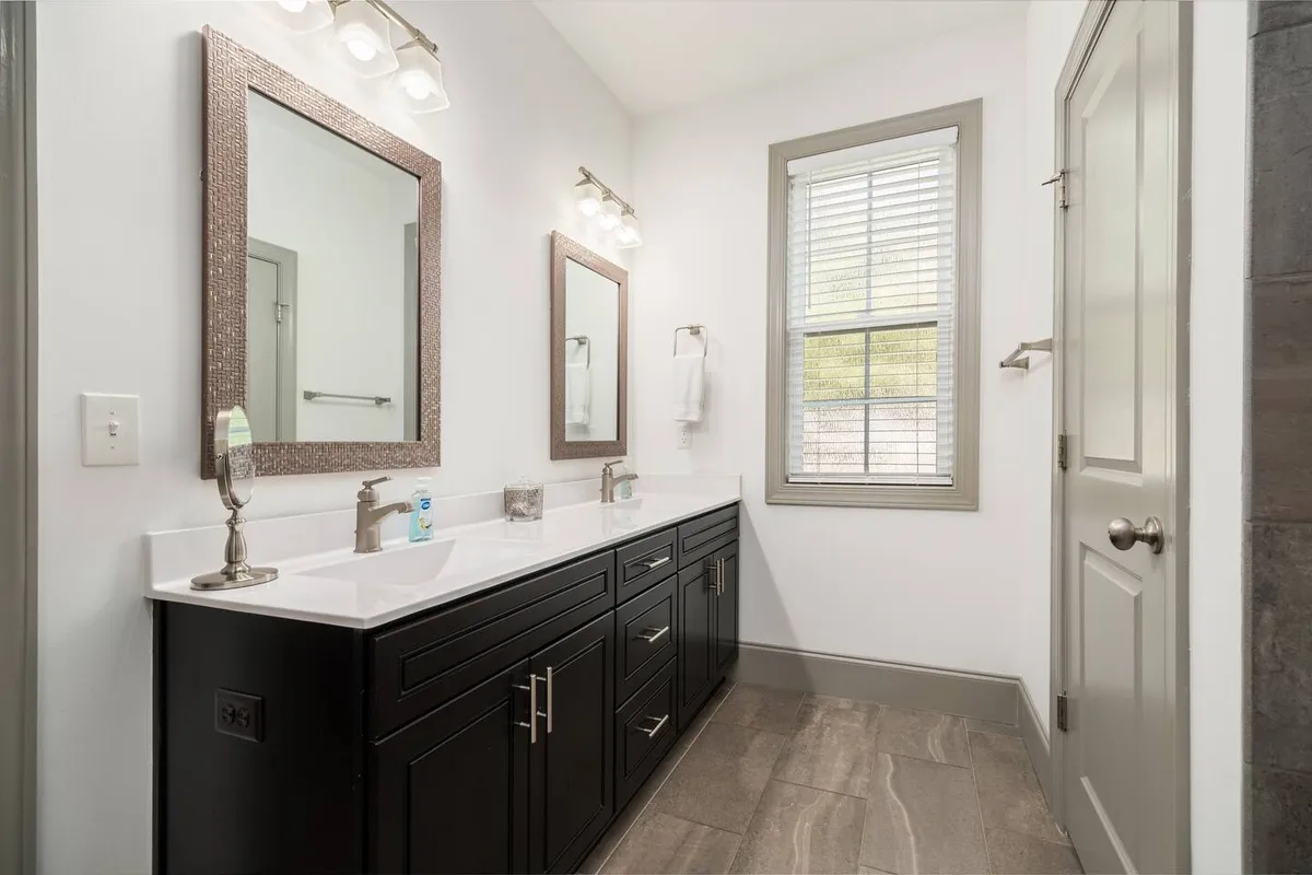 This calming and inviting interior scene showcases a double sink vanity with large mirrors and a window letting in natural light. The setup is designed for personal grooming and relaxation, evoking a sense of privacy and comfort perfect for self-care routines.