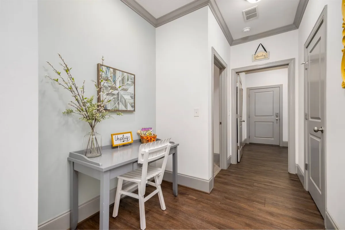 A tranquil nook featuring a small desk with a chair, a decorative vase with flowers, framed artwork, and a sign that reads 'Unplug'. The setup invites moments of relaxation, reflection, or quiet conversation, illuminated by gentle natural light.